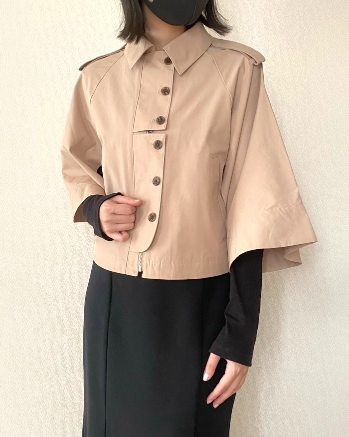 ベージュのコートを着た女性が黒いマスクを着用し、黒いドレスと合わせたスタイルを披露しています。