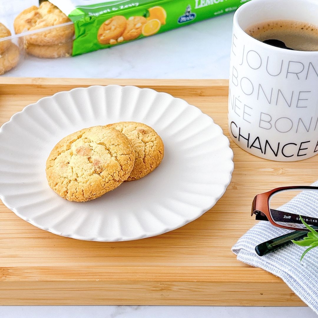 白い皿にクッキーが2枚乗っており、隣にコーヒーの入ったマグカップと眼鏡が置かれた整理されたテーブル。