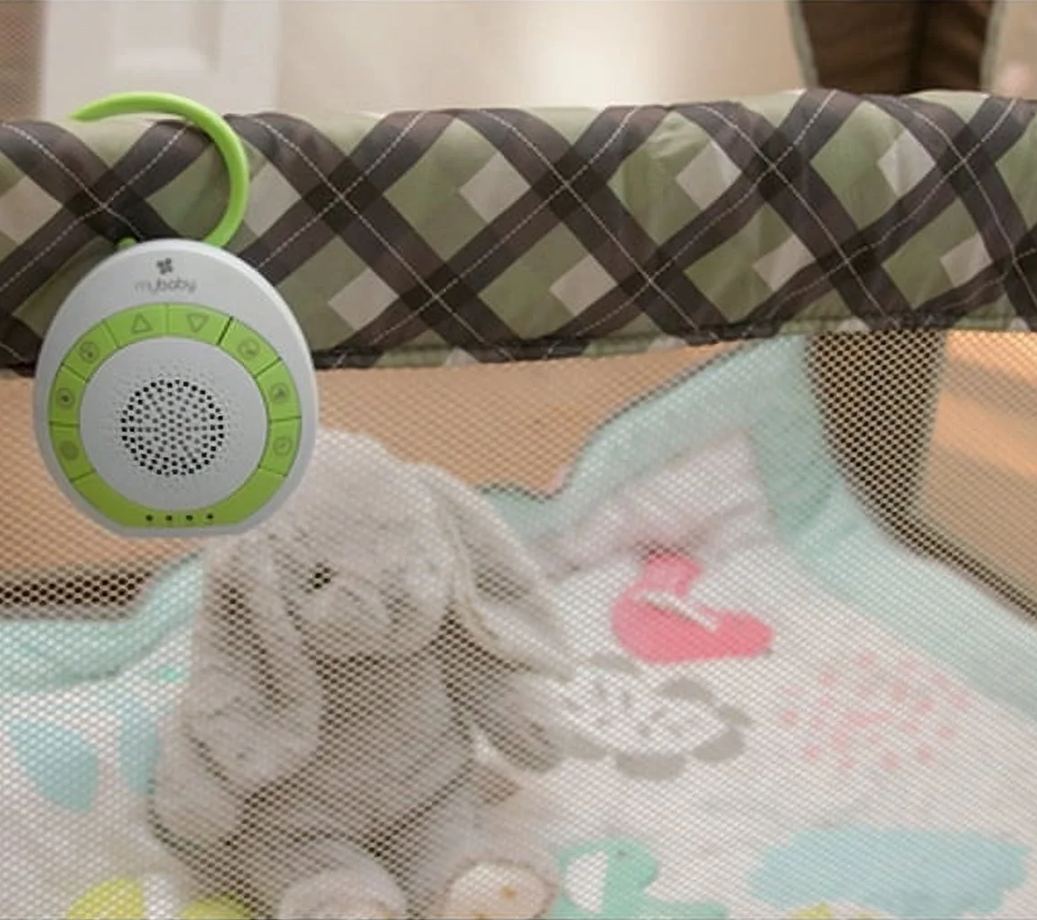 Portable baby sound machine with green trim attached to playpen, accompanied by a plush toy on a patterned baby mat
