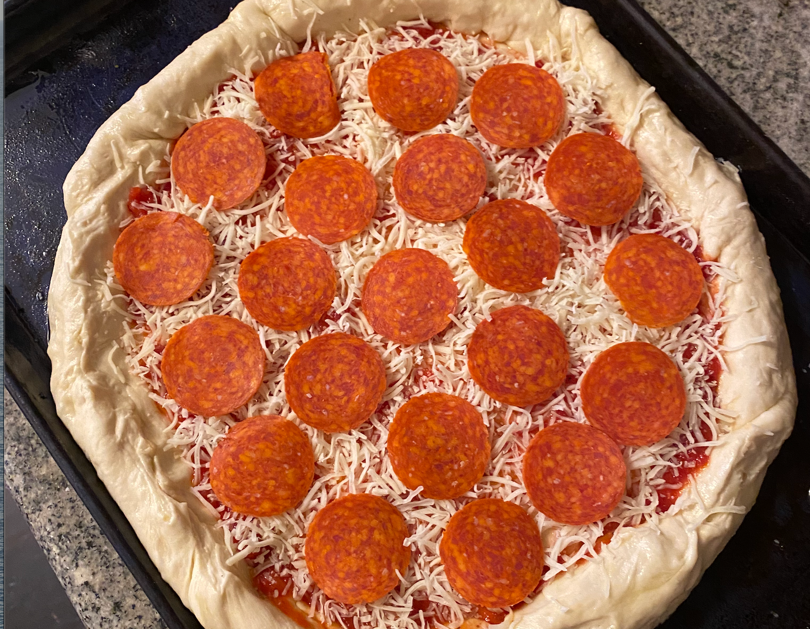 Unbaked pizza topped with shredded cheese and pepperoni slices, set on a baking tray