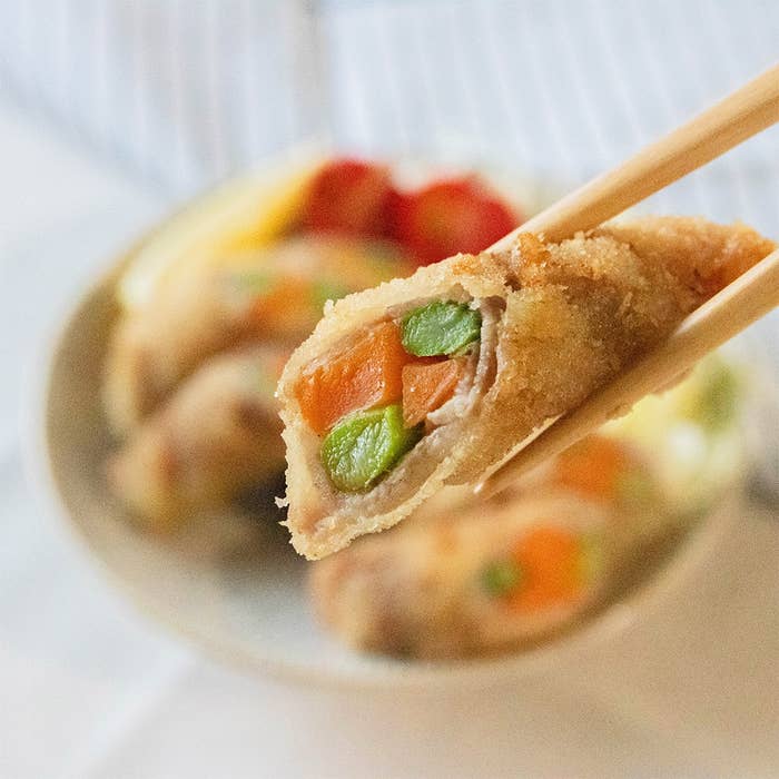 箸で持たれたアスパラガスとにんじんの肉巻きフライ。