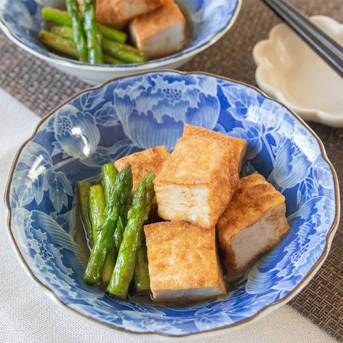 青い模様の皿に載った厚揚げとアスパラの料理。背景に箸と小皿が見える。