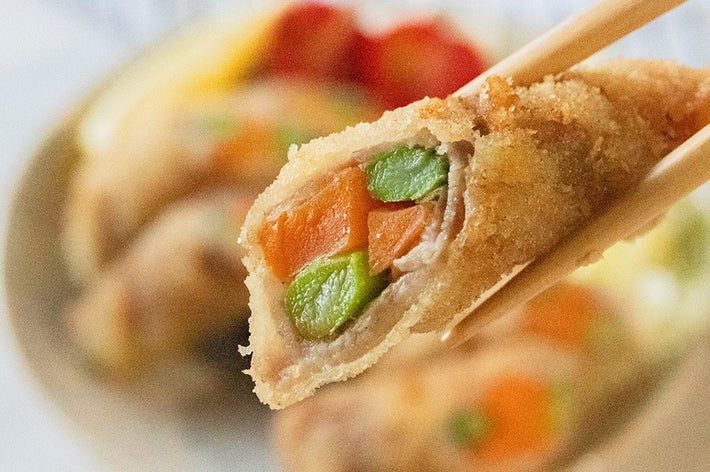 箸で持たれたアスパラガスとにんじんの肉巻きフライ。