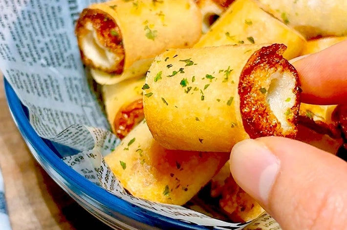 指で持たれたサクサクの春巻き。中にチーズが入っている。新聞の上に盛り付けられている。