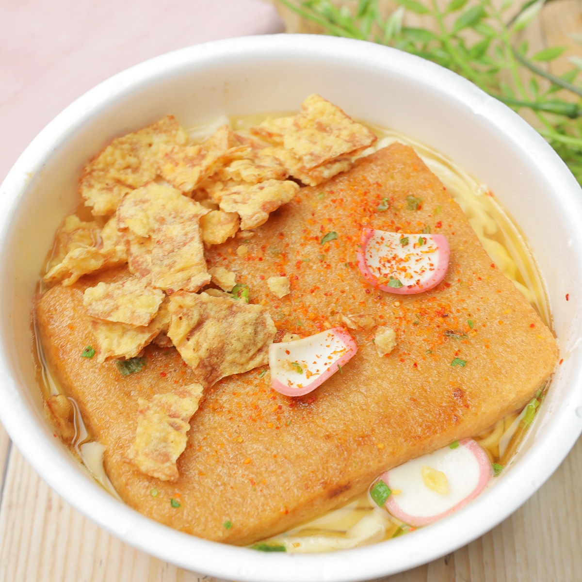 うどんの上に揚げ、かまぼこ、薬味が載った料理が白い器に盛られている。