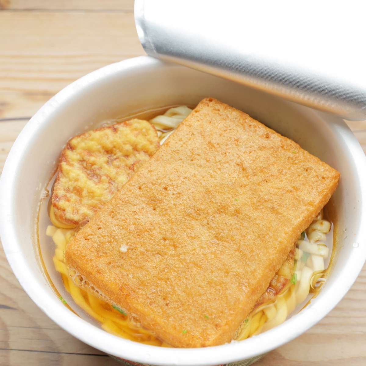 蓋が半開きのカップ麺、揚げが乗った状態で中に麺とスープが見えます。