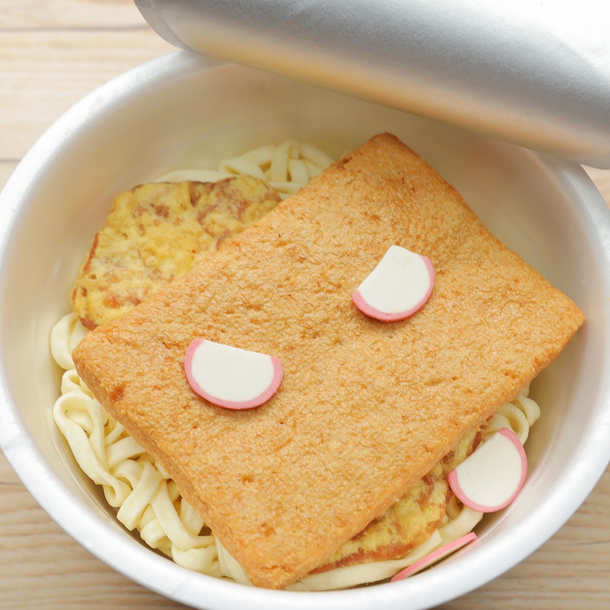 蓋を開けたカップうどんの中に、うどん、揚げ、かまぼこが入っている。