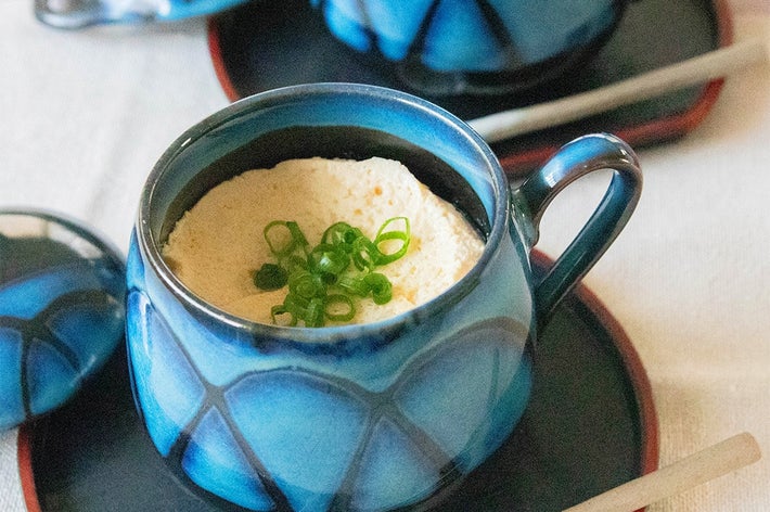 青い陶器カップに入った茶碗蒸しが2つ、ネギがのっている。カップ横に小さなスプーンが添えられている。