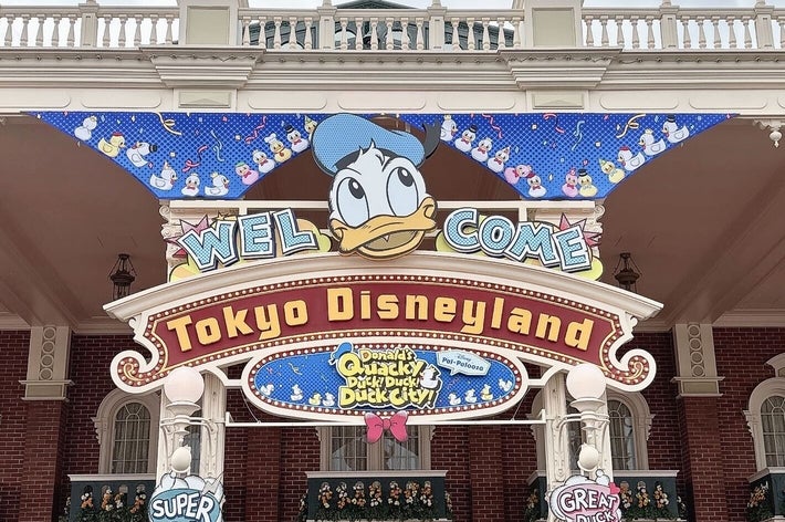 東京ディズニーランドのエントランスで、ドナルドダックが描かれた「ようこそ」のサイン。観客が下に集まっている。