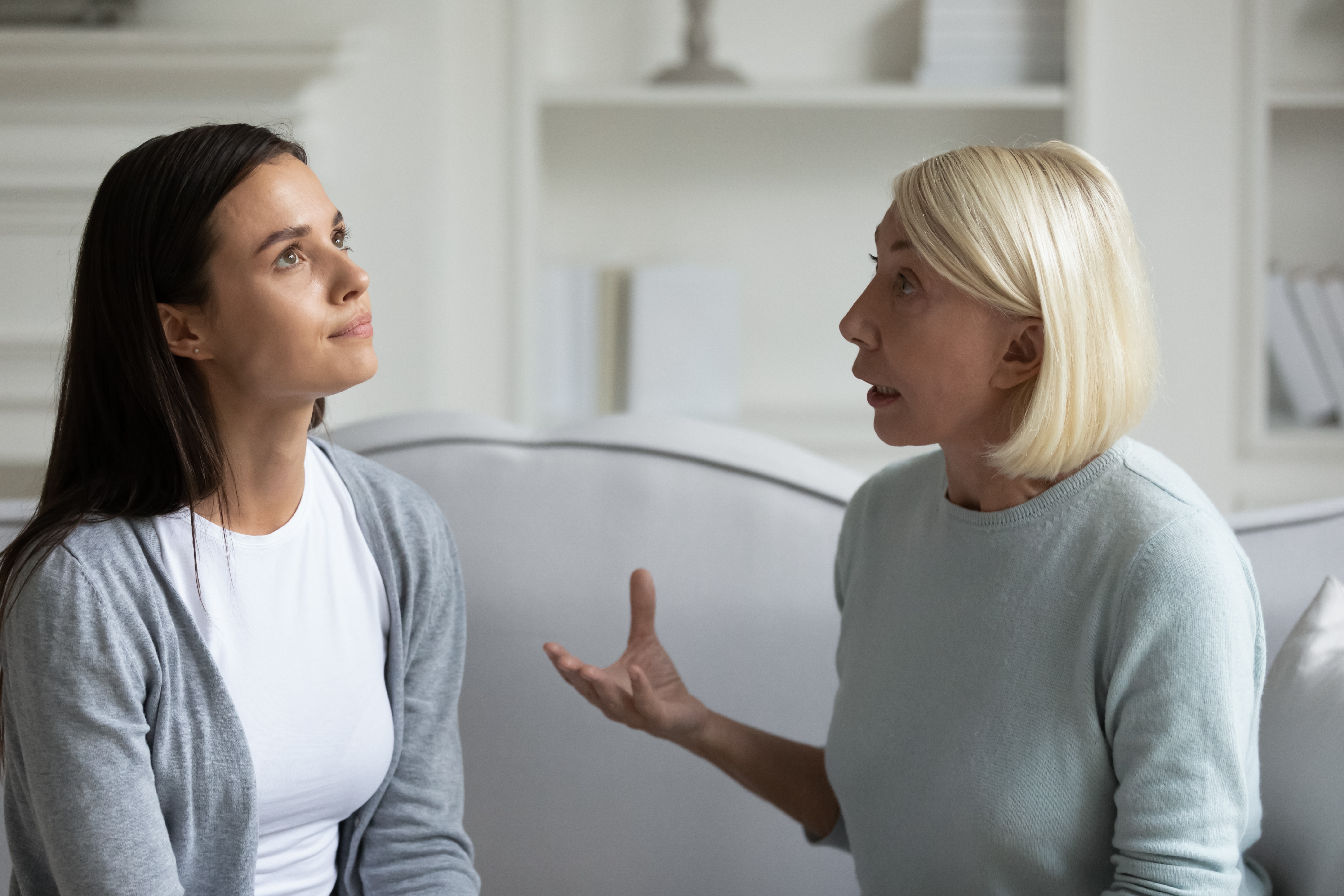 Two women sitting on a couch engaged in a serious conversation, one gesturing expressively while the other listens attentively