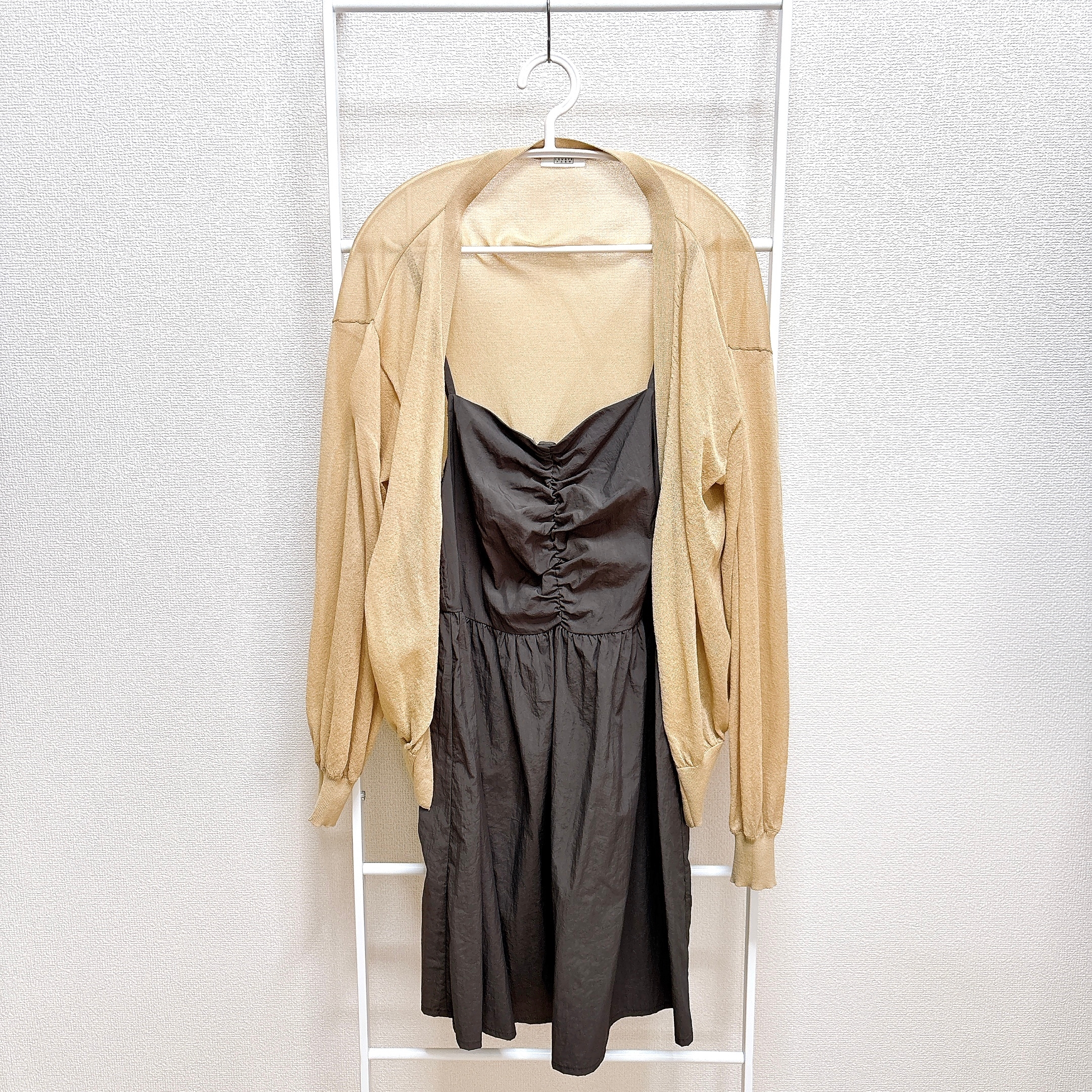 黒のドレスに、ベージュのカーディガンが重ねられている。服はハンガーにかけられている。