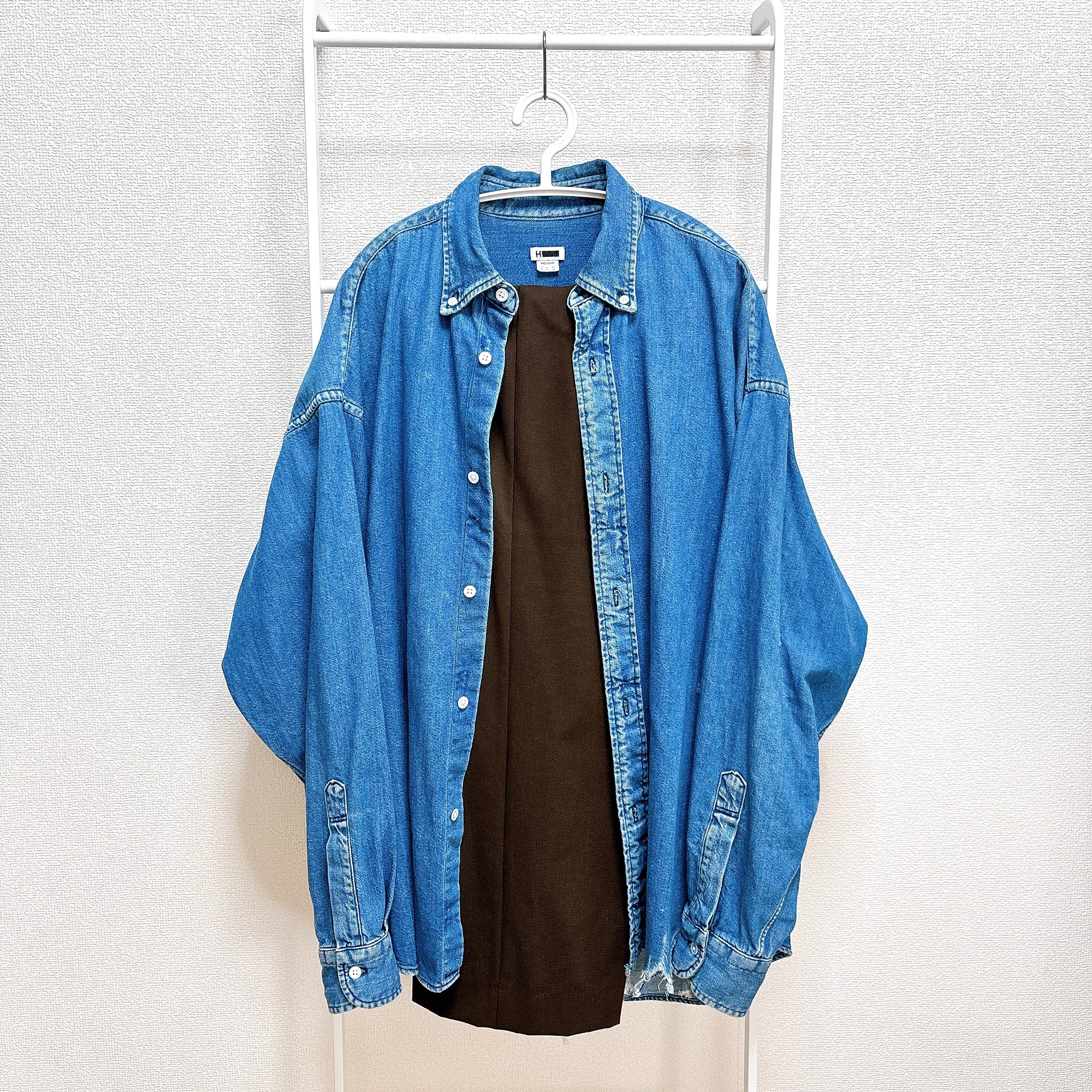 デニムシャツがハンガーに掛けられ、下に黒いシャツが重ねられています。シンプルでカジュアルなスタイル。