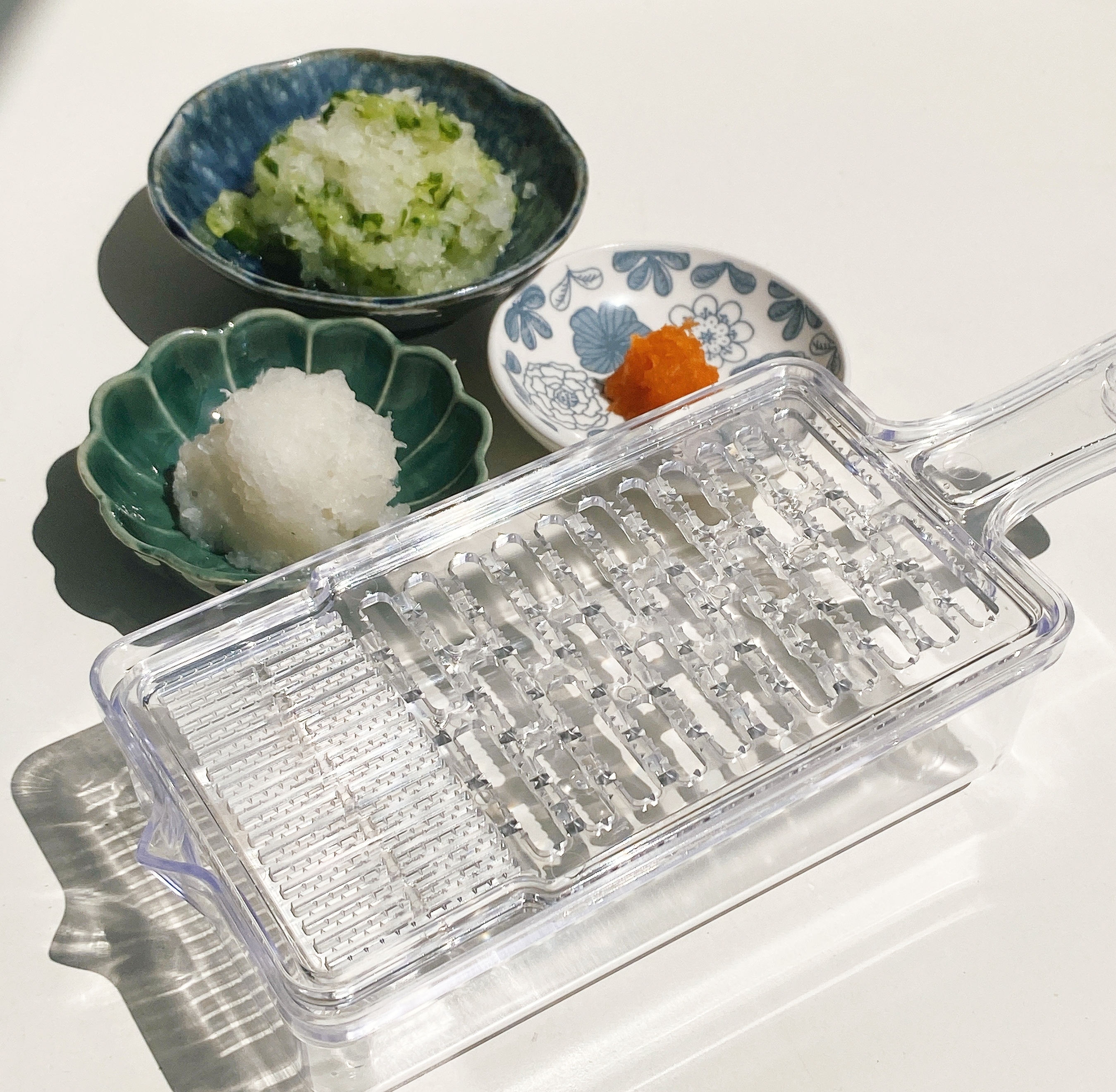 すりおろし器と3つの器に盛られた大根おろし、ねぎ、唐辛子。