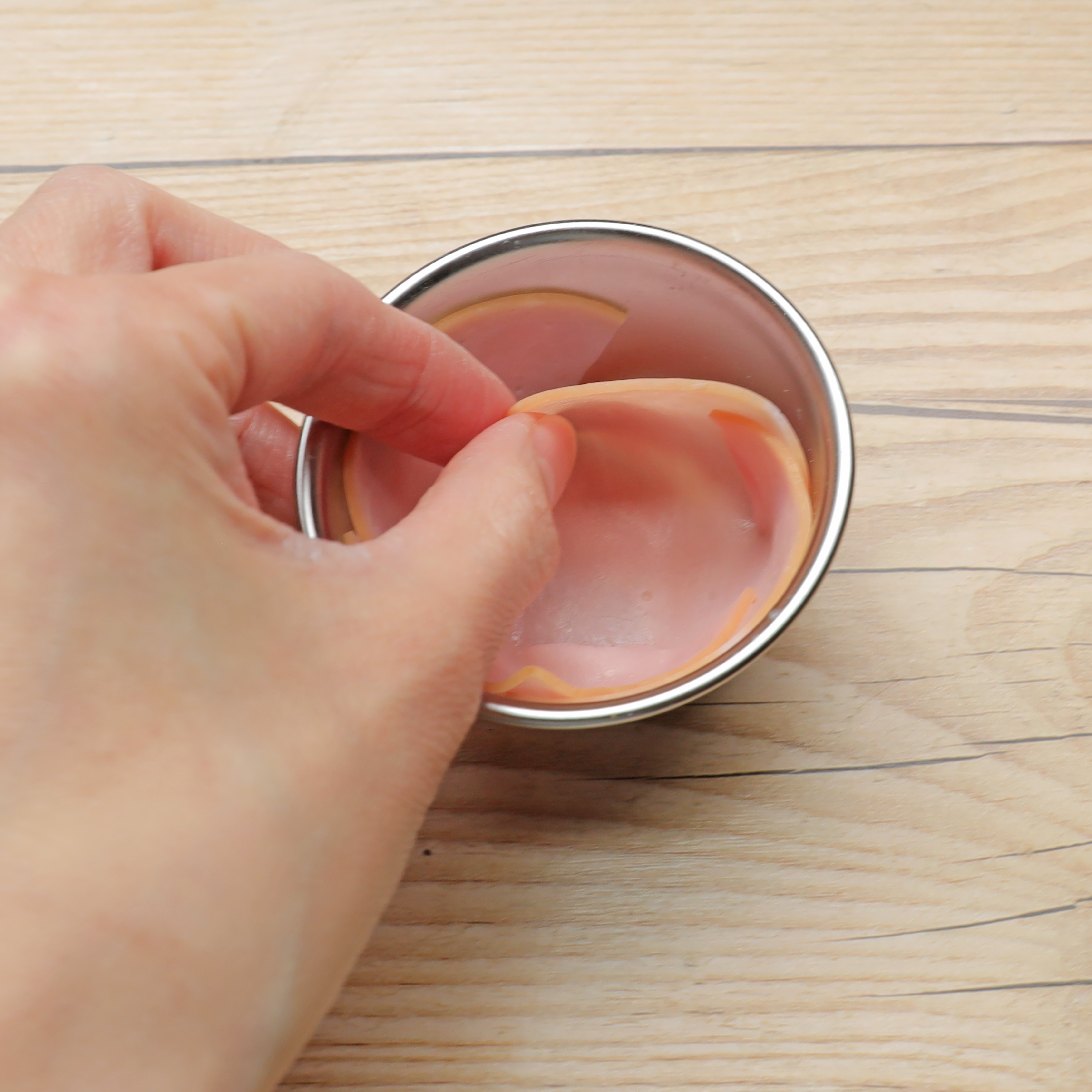 手が金属製の容器のハムスライス