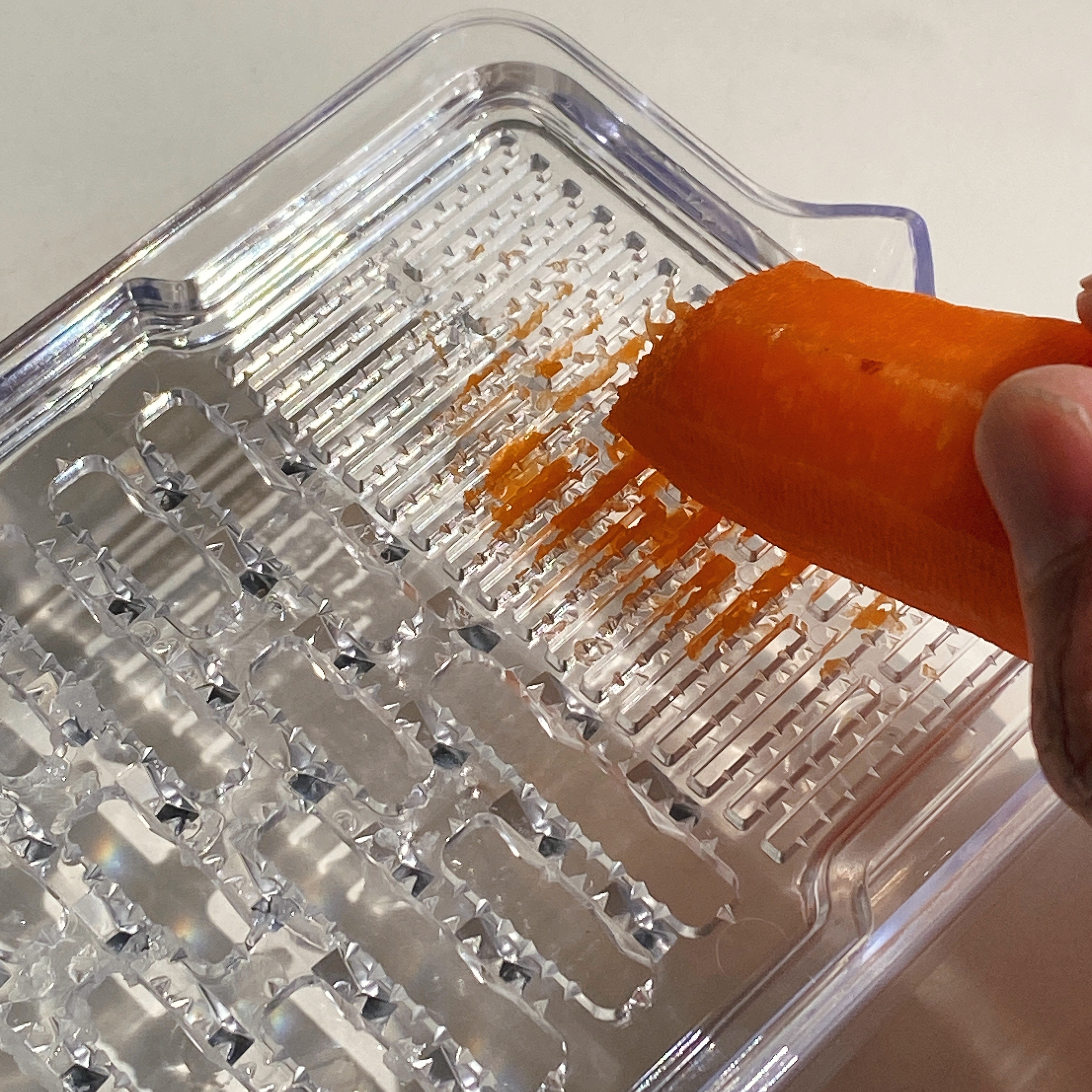 手で持ったニンジンがおろし器ですりおろされている様子。透明なケースにすりおろしたニンジンがたまっている。