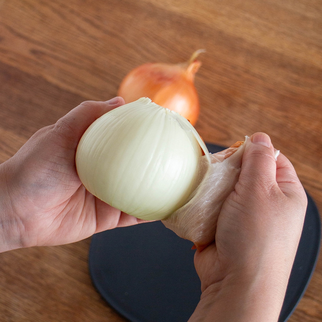 人が玉ねぎの皮を剥いている様子。背景にもう一つの玉ねぎが見える。