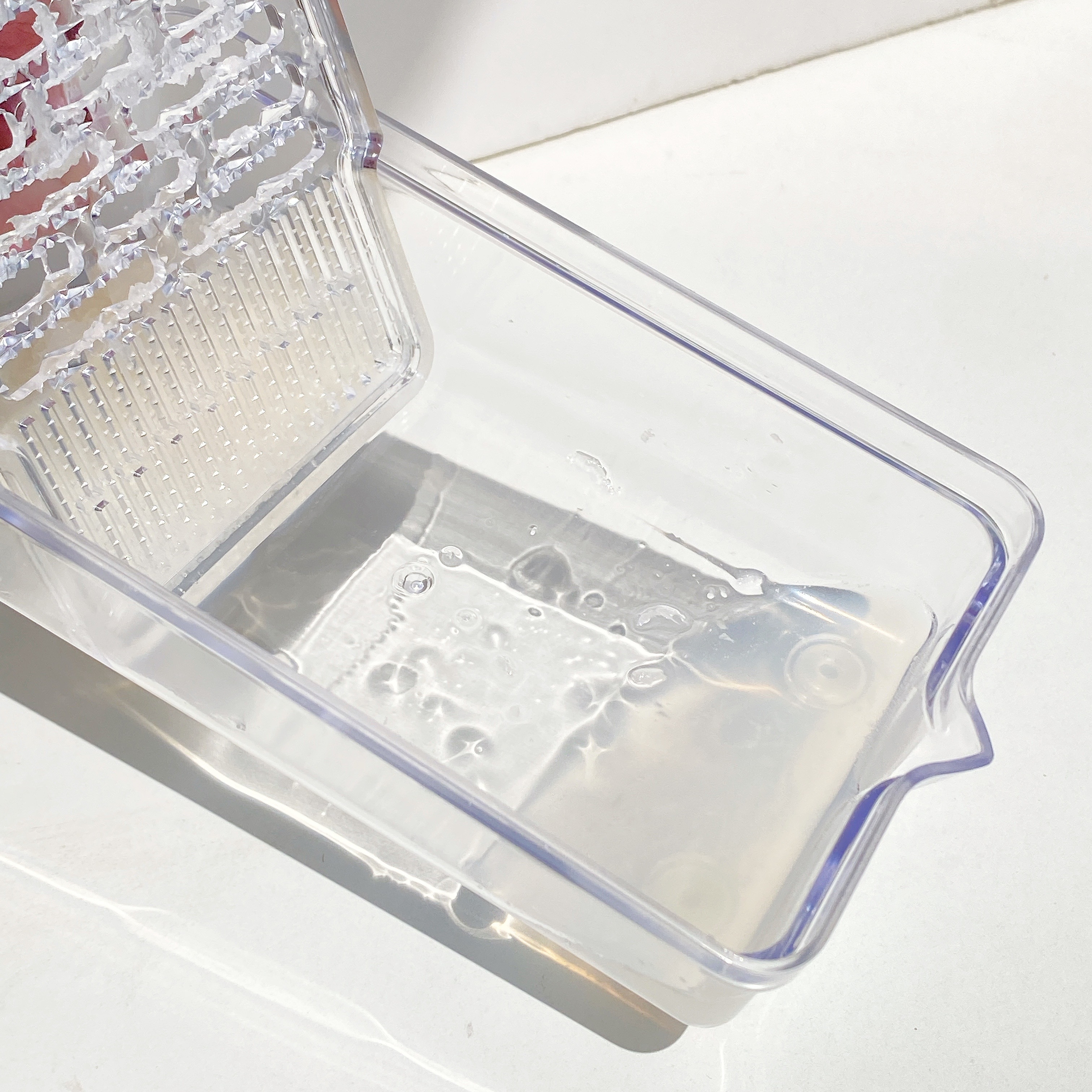 透明なプラスチック容器に液体が少量入っています。容器にはすりおろし器が一体化されています。