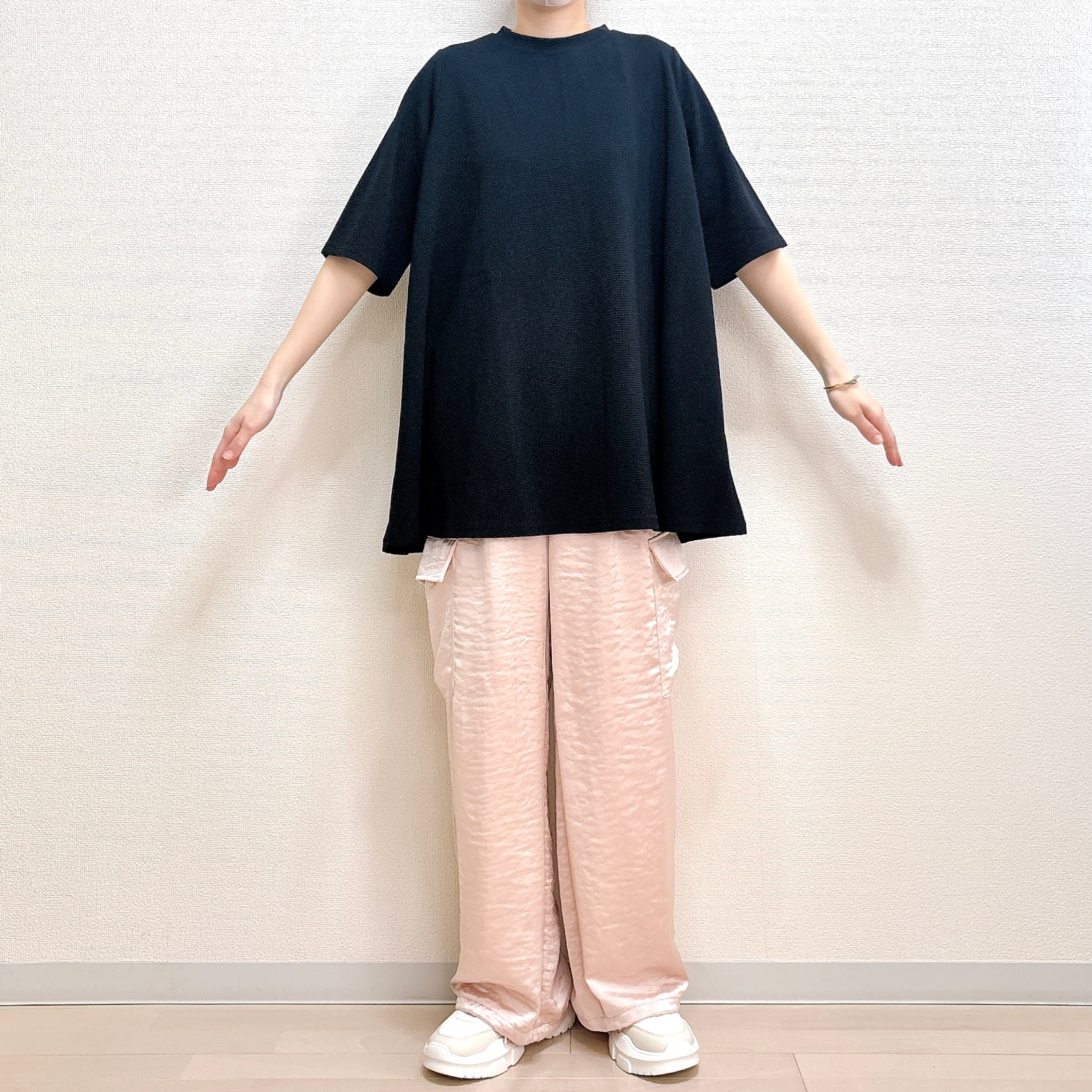 黒いオーバーサイズのトップスとゆったりした白いパンツを着た人物が直立している。