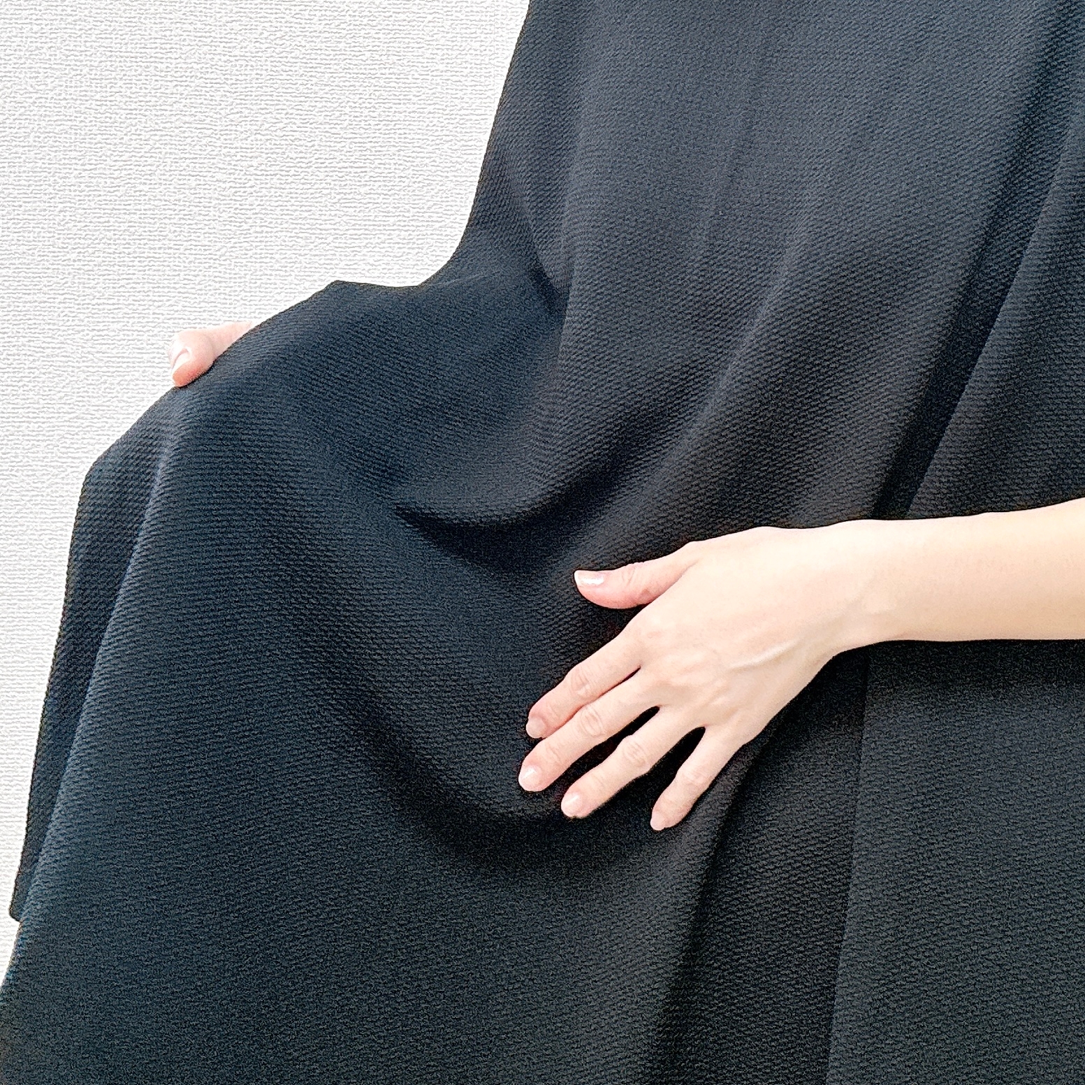 人物が黒い布を手で軽く持ち上げている様子。
