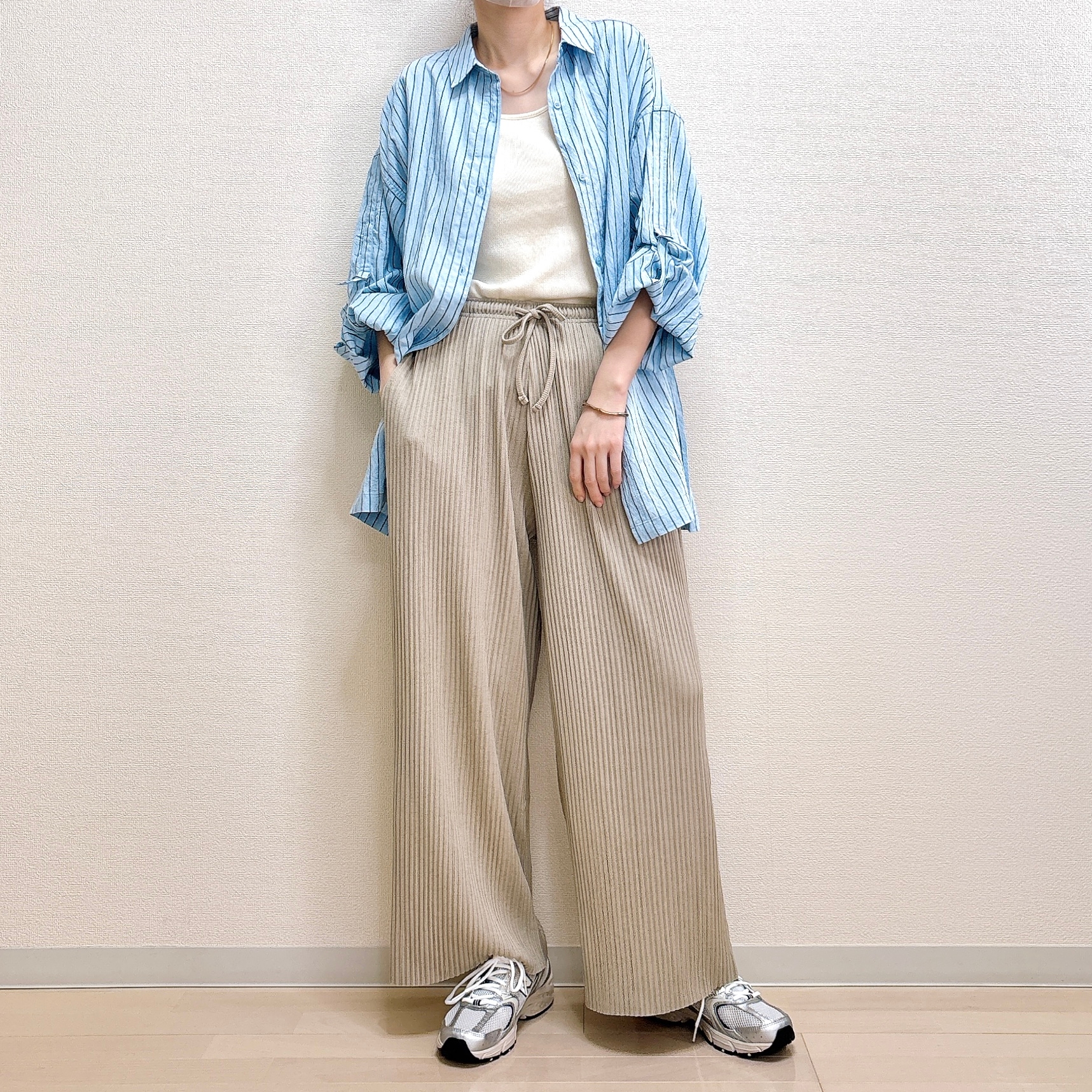 ゆったりしたストライプシャツとルーズなパンツを履いた人物がカジュアルなスタイルで立っている。