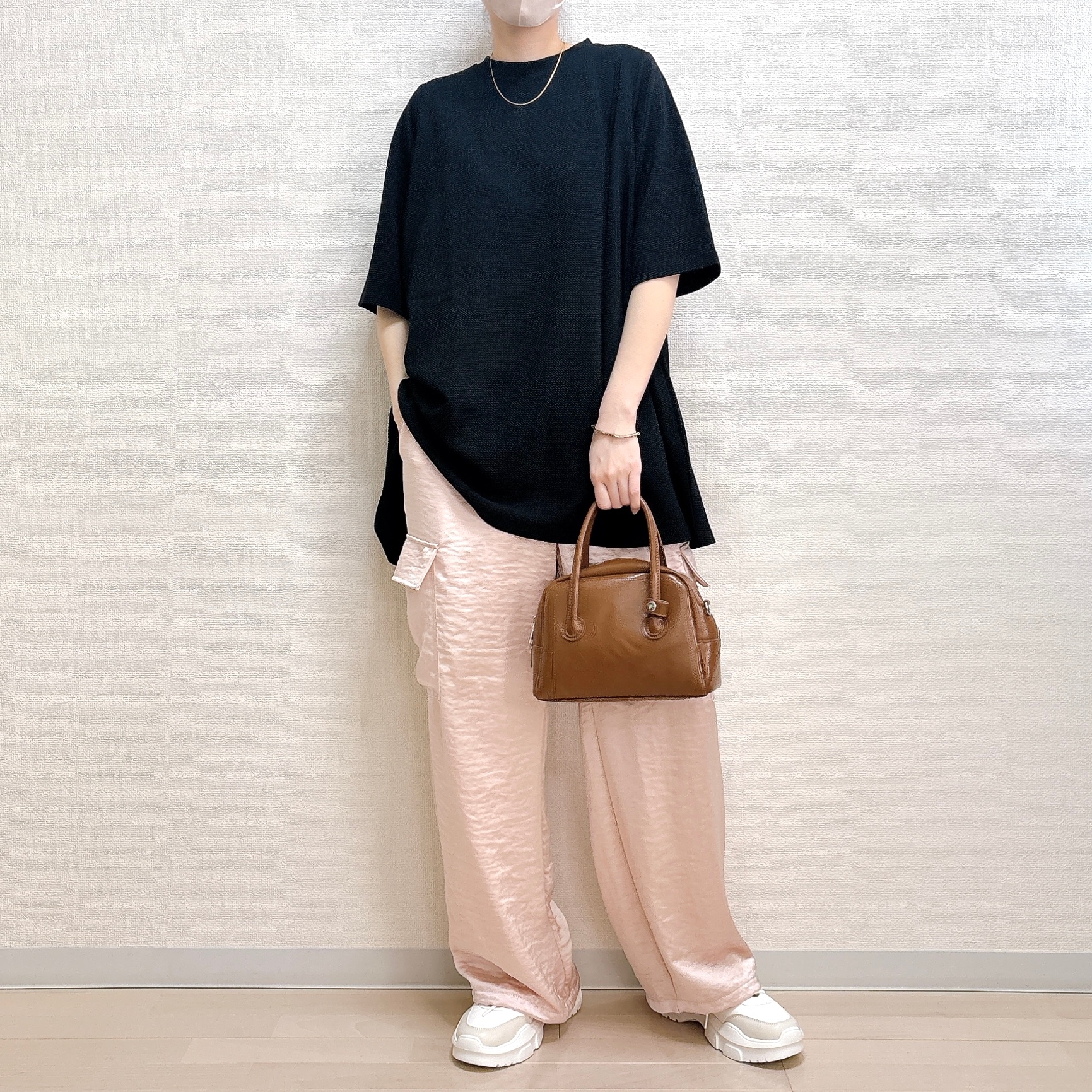 黒のゆったりしたトップスと、ピンクのワイドパンツを着た人物が、ブラウンのハンドバッグを持っている。