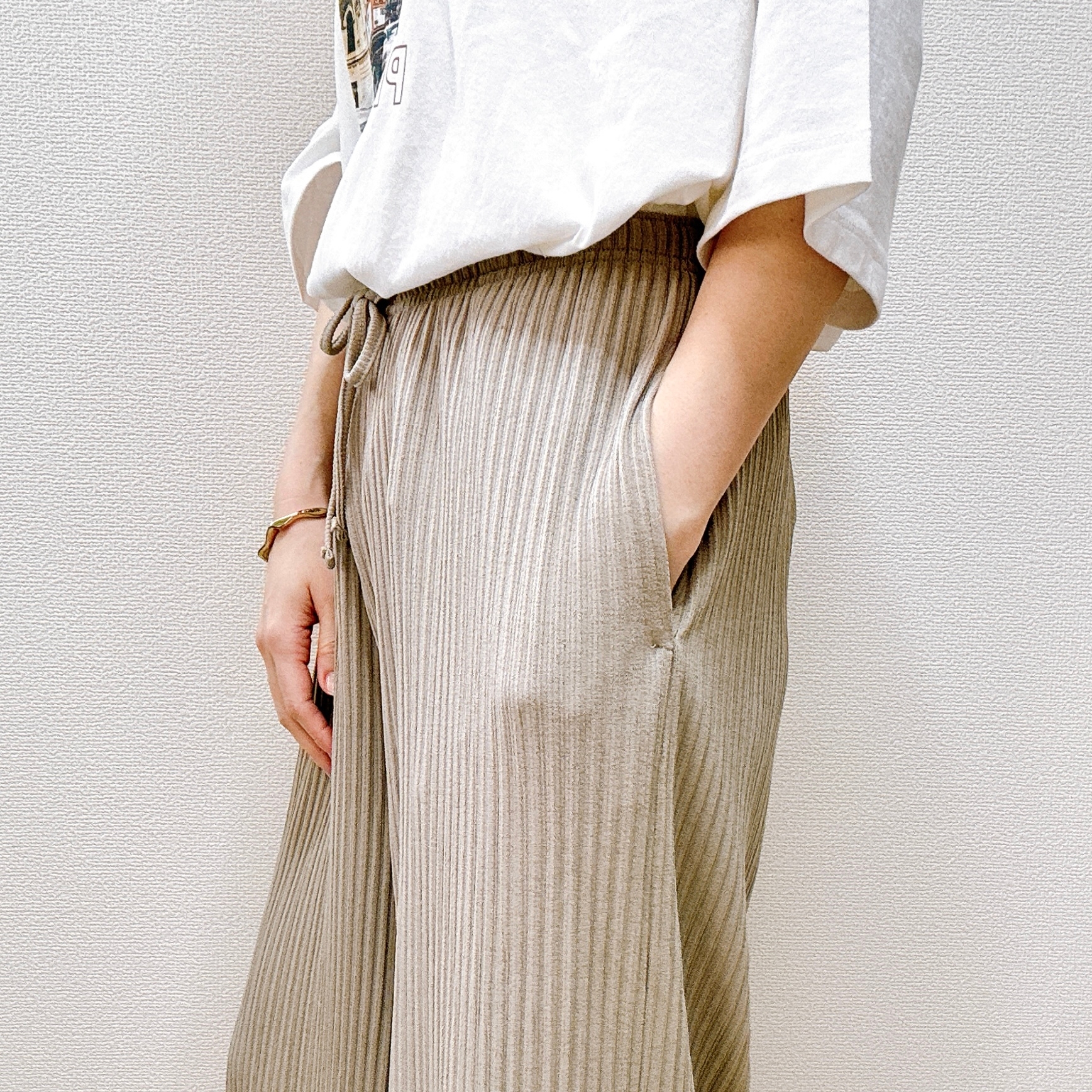 人物がカジュアルなリブパンツとTシャツを着用し、手をポケットに入れている姿。