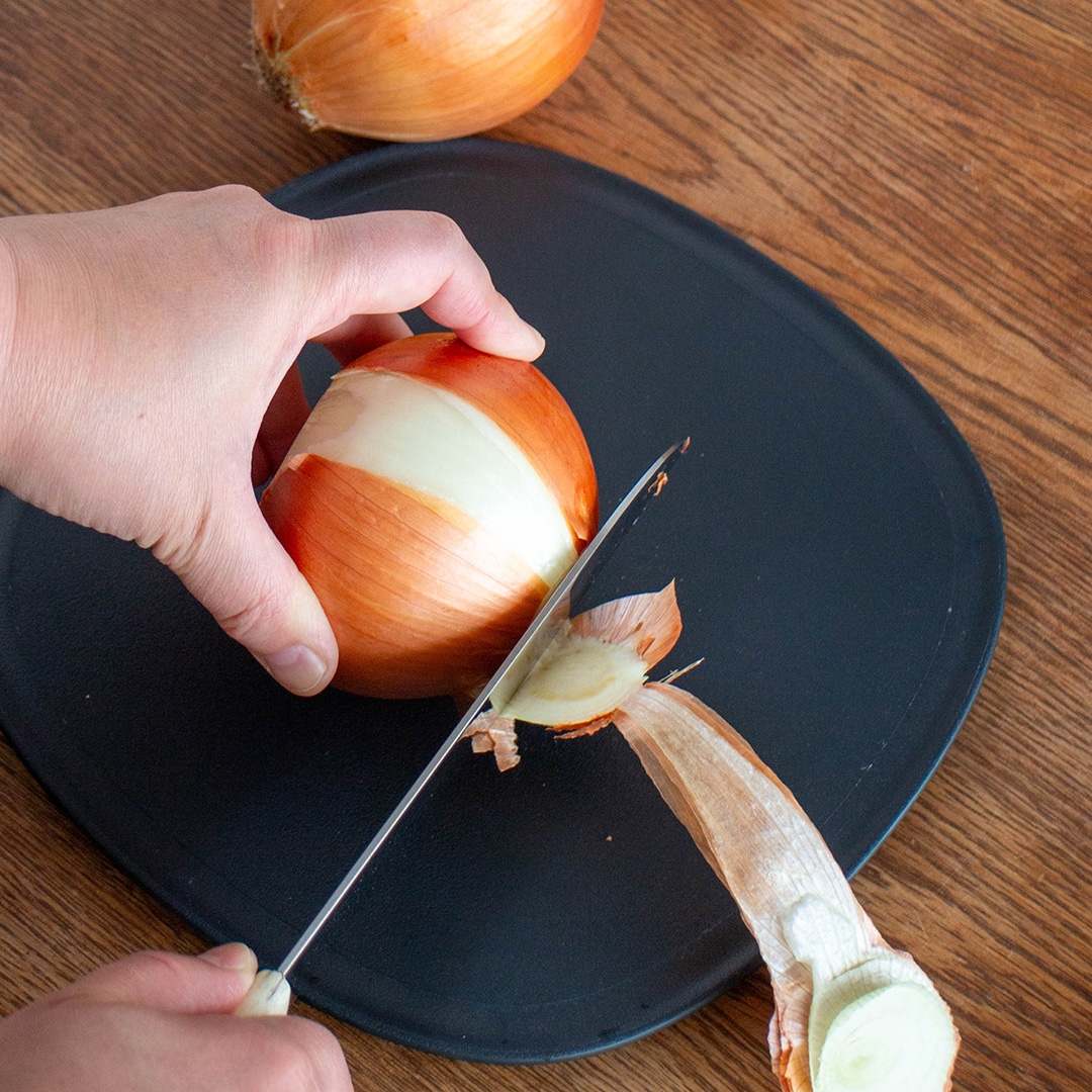人がまな板の上で玉ねぎの皮を剥きながら切っている様子。