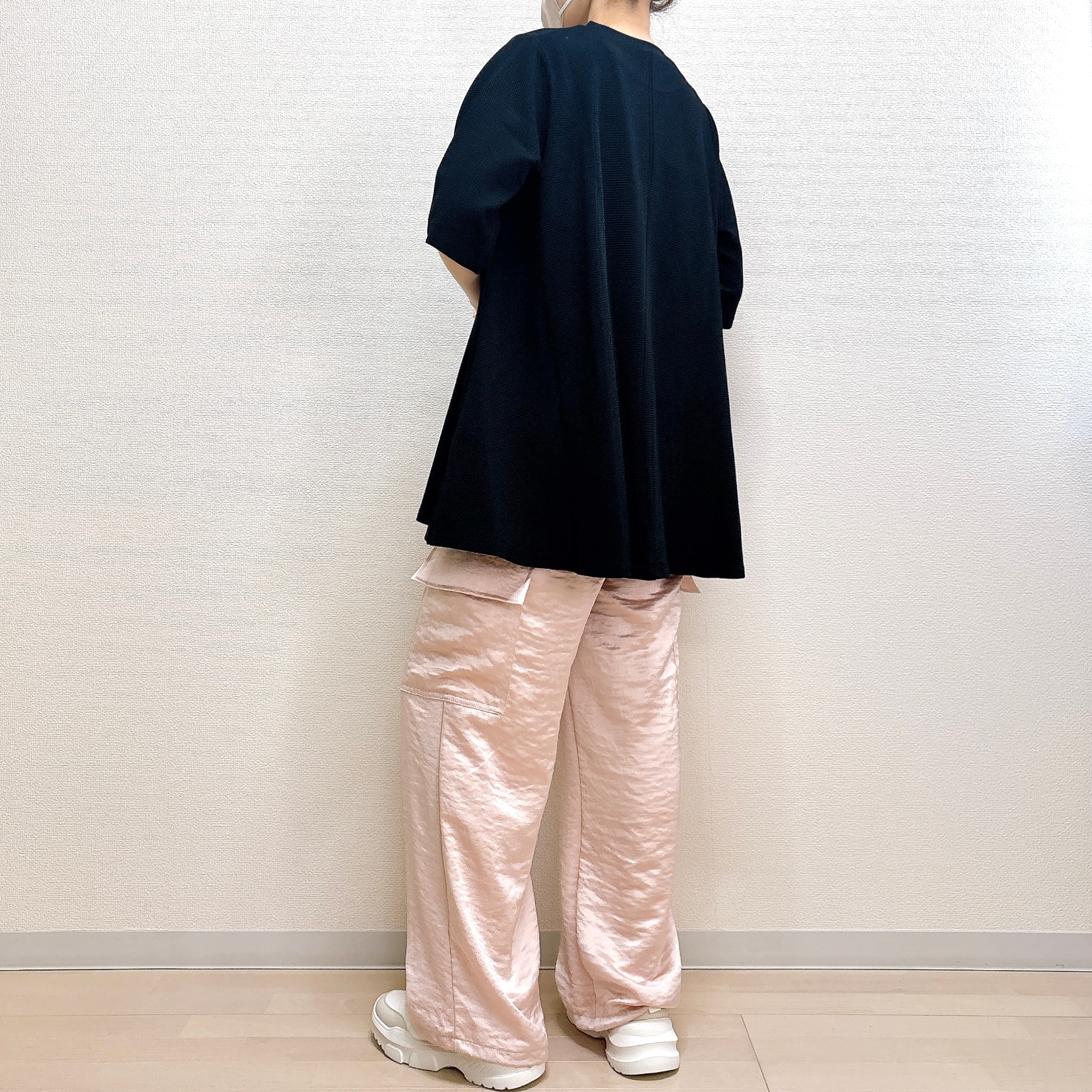 背を向けた人が黒いトップスとゆったりしたパンツ、白いスニーカーを着用しています。