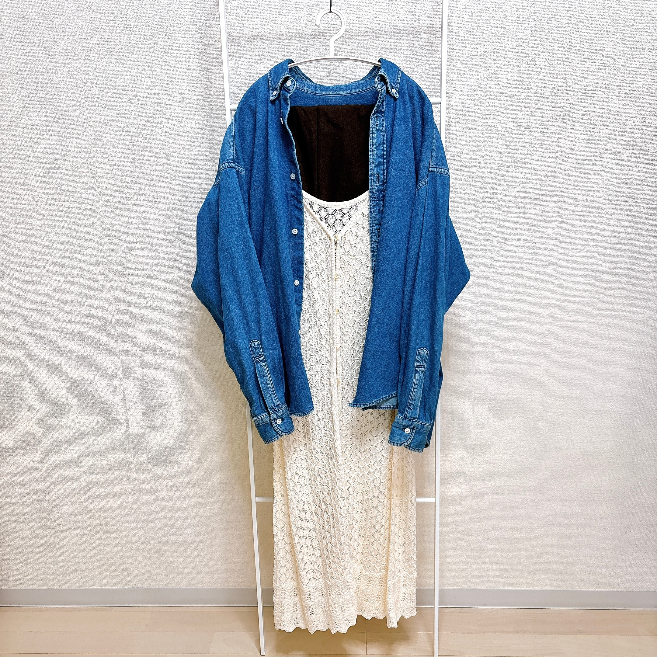 ハンガーに掛けられたデニムシャツと繊細な編み模様の白いロングワンピース。カジュアルスタイルのコーディネート。