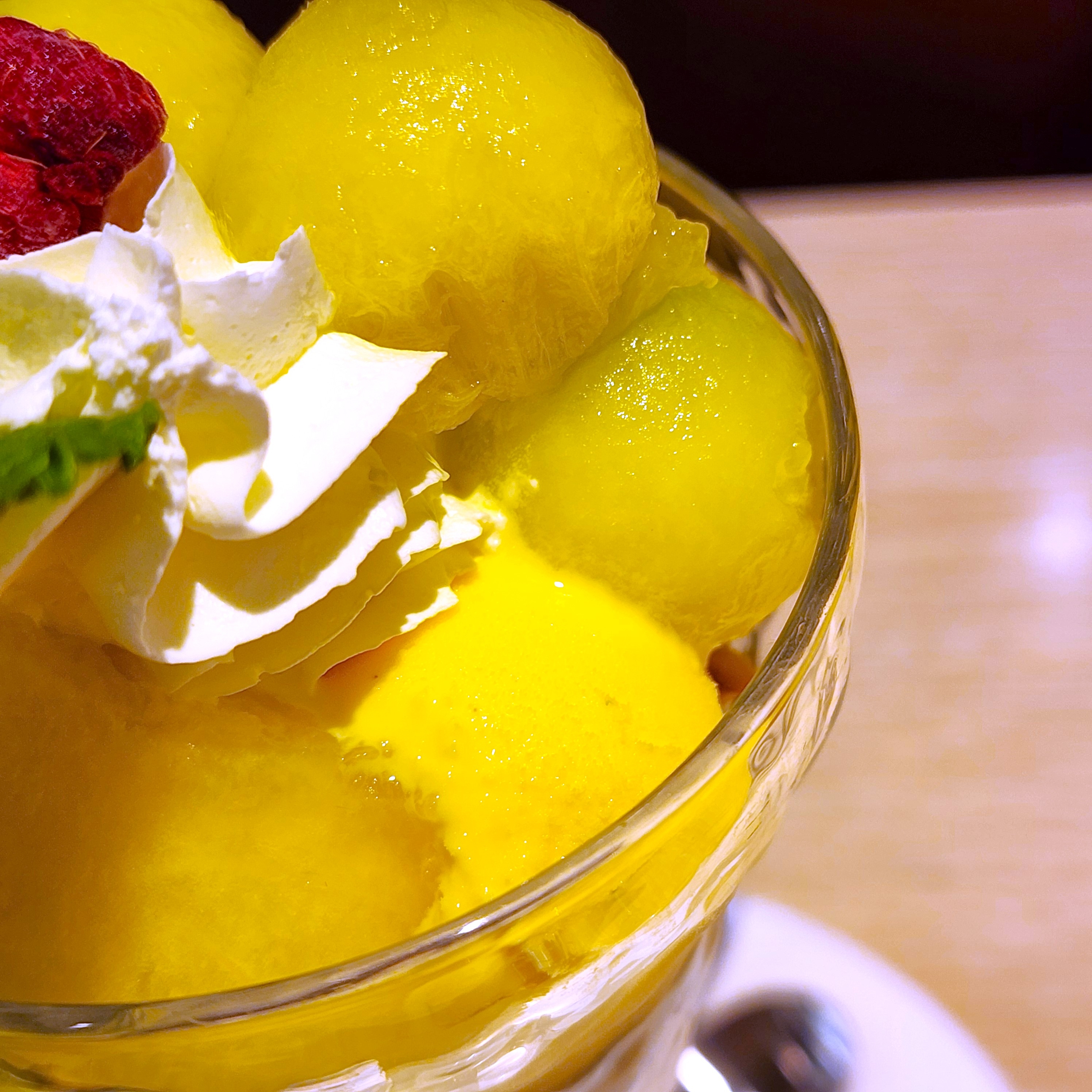 クリームとラズベリーがトッピングされたメロンボールとマンゴーのパフェ。