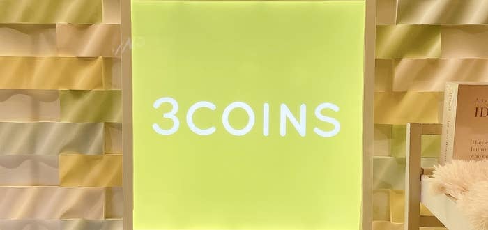 壁に設置された「3COINS」の看板。周囲にはデコラティブな波状の装飾が施されている。