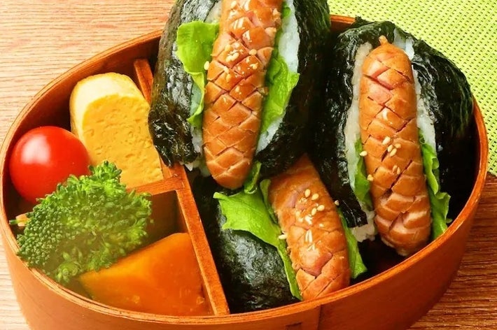 お弁当箱に海苔巻きおにぎり3個、ウインナー、卵焼き、ブロッコリー、カボチャ、ミニトマトが詰まっている。
