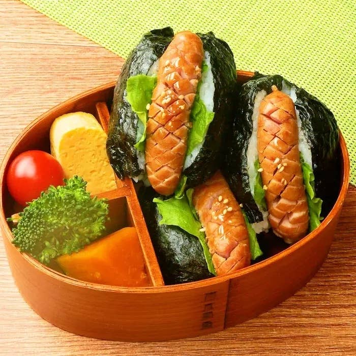 お弁当箱に海苔巻きおにぎり3個、ウインナー、卵焼き、ブロッコリー、カボチャ、ミニトマトが詰まっている。