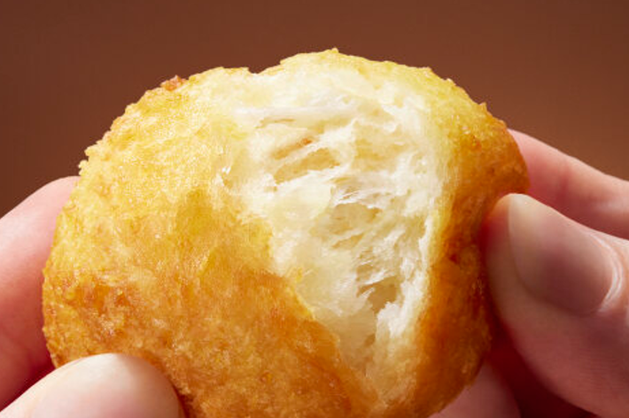 手で持たれたサクサクとした揚げたパンの一部がかじられている様子。食感が特徴的。