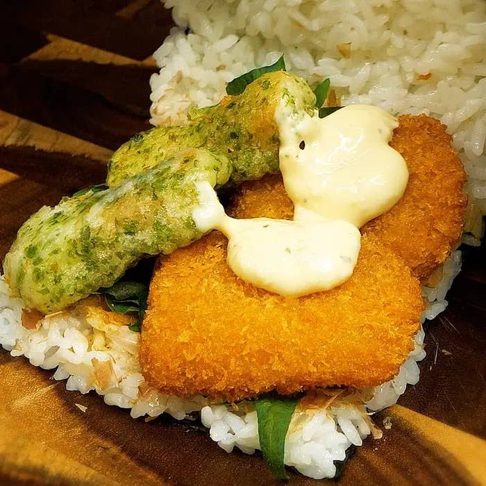 ご飯の上に揚げた魚のフライと天ぷらが載っている様子。