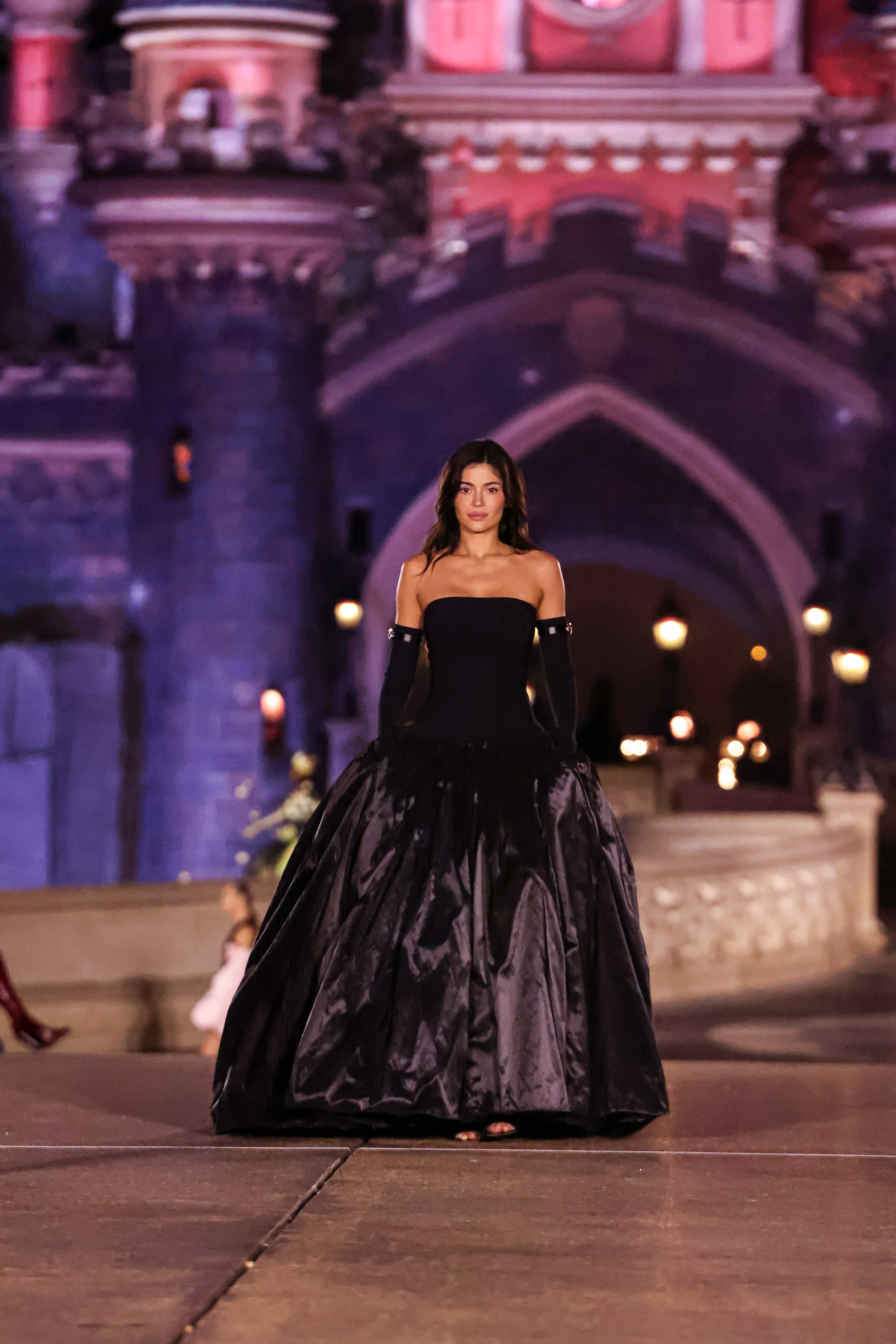 Kylie Jenner in a dramatic black evening gown in front of a castle backdrop at night