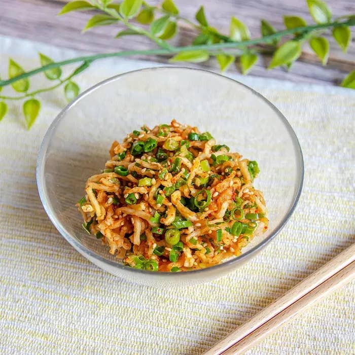 ガラスのボウルに盛られたアジアン風の切り干し大根サラダ。青ネギがトッピングされ、棒状の箸が近くに置かれている。