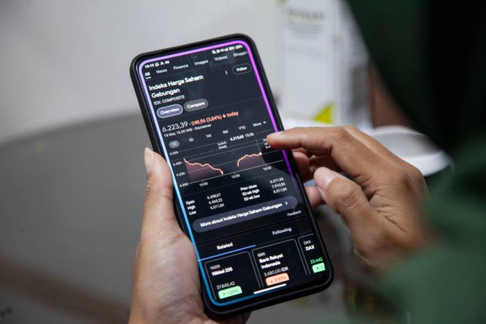 Person using a smartphone to check stock market data, with charts and financial figures visible on the screen