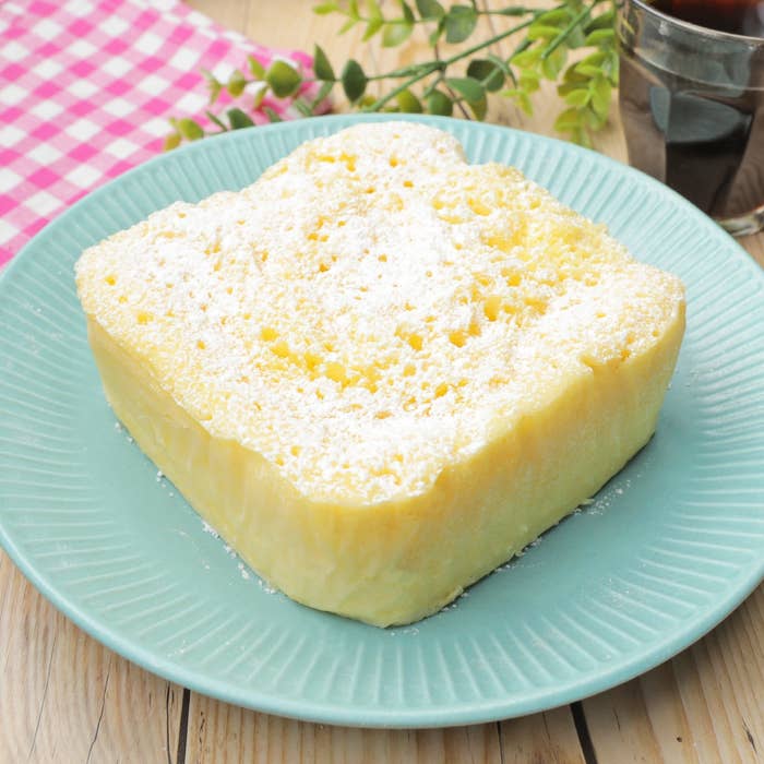 お皿に四角いケーキがあります。上に粉砂糖がかかっており、飲み物があります。