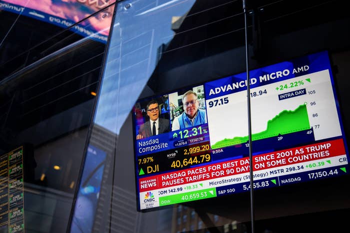 Stock market data displayed on a large screen, showing a news broadcast about Nasdaq and Dow Jones Index fluctuations