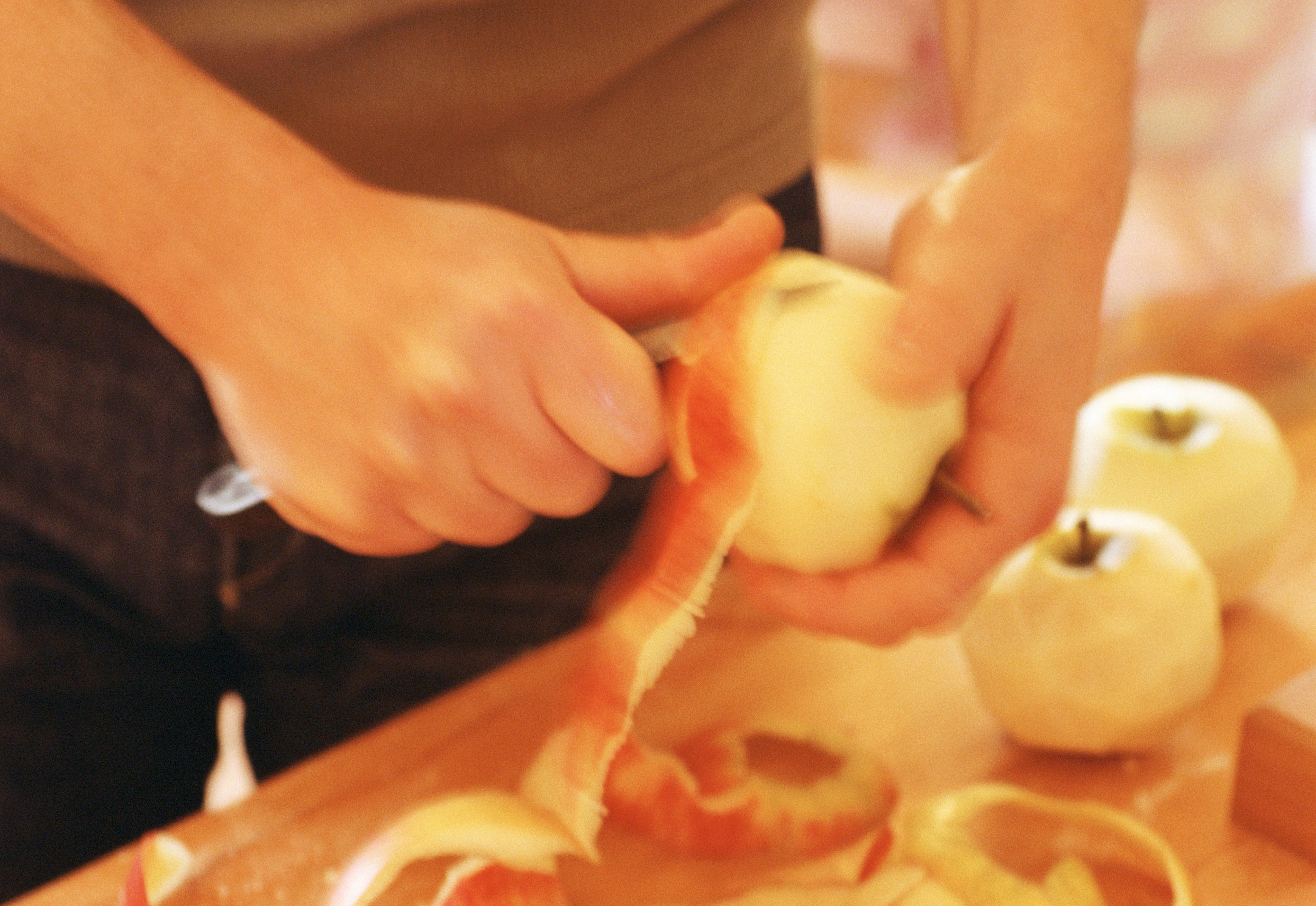 Person peeling apples on a wooden surface, surrounded by apple peels and whole apples