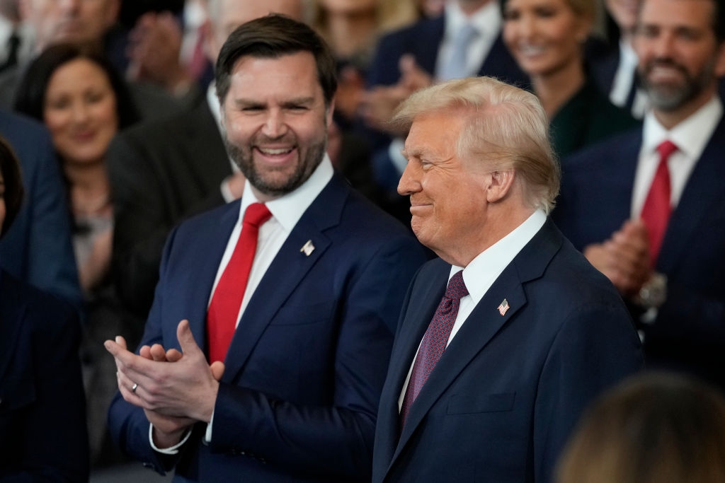 Two individuals in suits smiling and applauding among a crowd at an indoor event