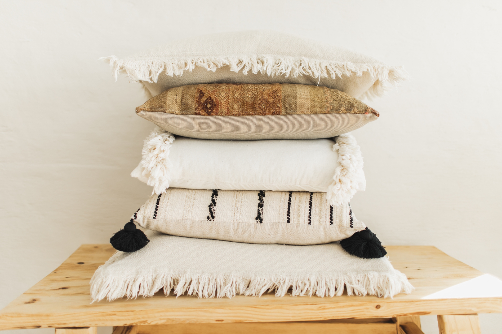 Stacked decorative pillows with tassels and fringe on a wooden bench, creating a cozy, layered look