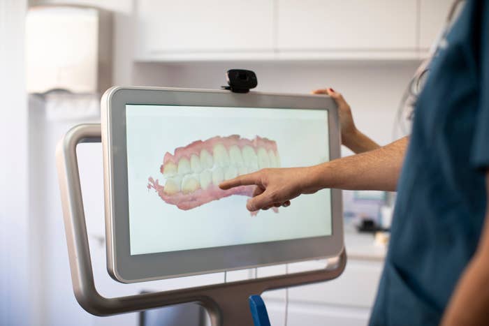 A dentist points to a digital display showing a 3D model of teeth in a dental office