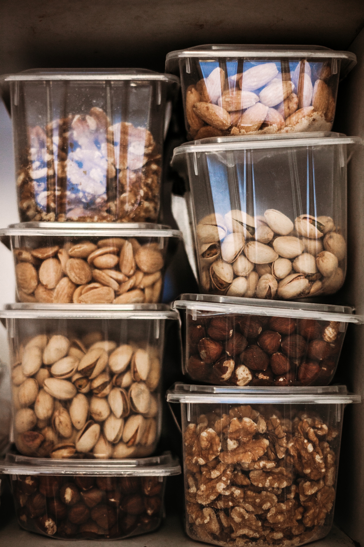Containers of various nuts stacked on shelves, including walnuts, pistachios, and hazelnuts