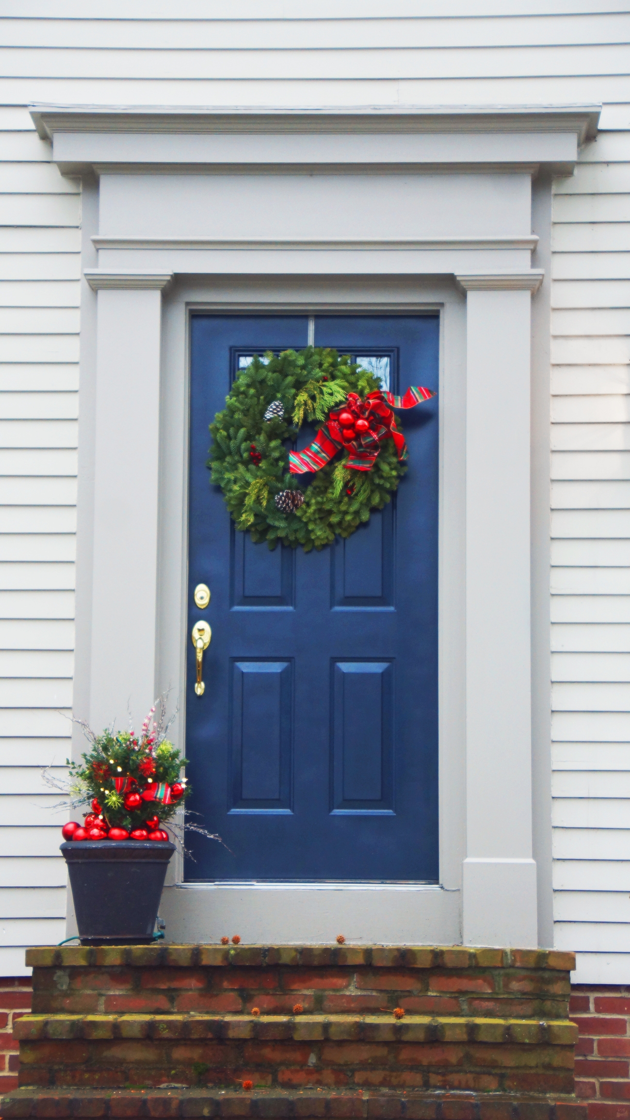 Festive front door with a lush wreath and a planter holding red decorations