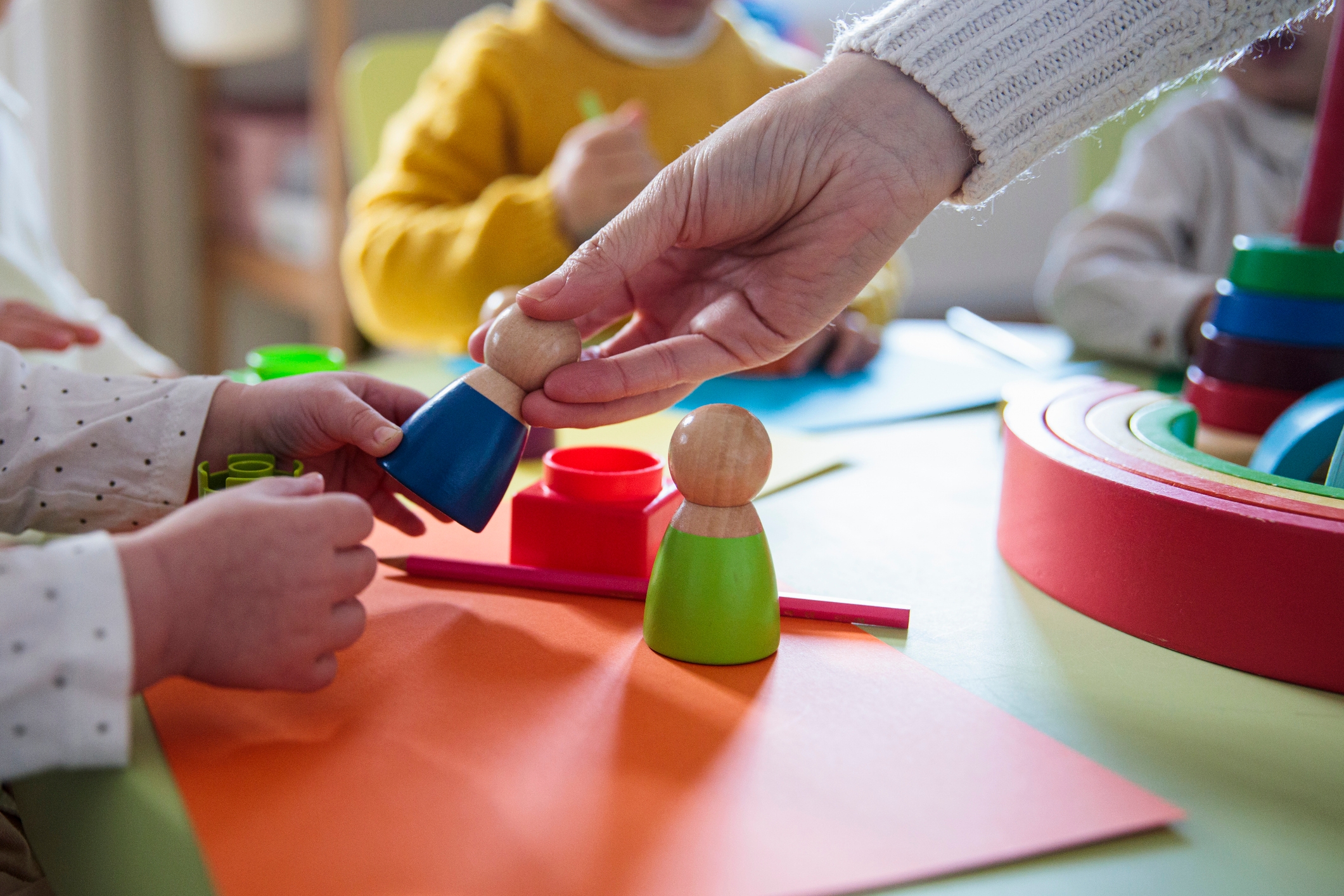 Children play with colorful toys on a table as an adult hand arranges the pieces