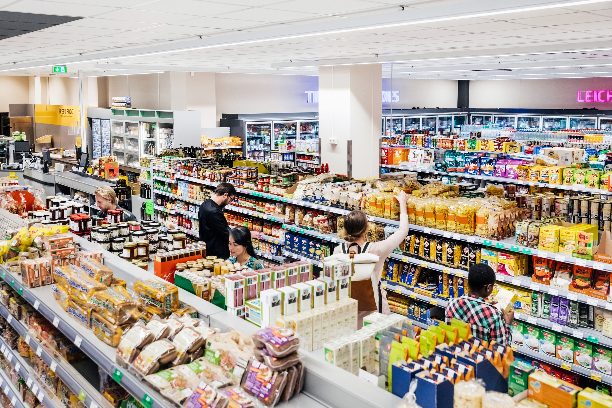 People shopping in a busy grocery store, browsing various food and household product aisles