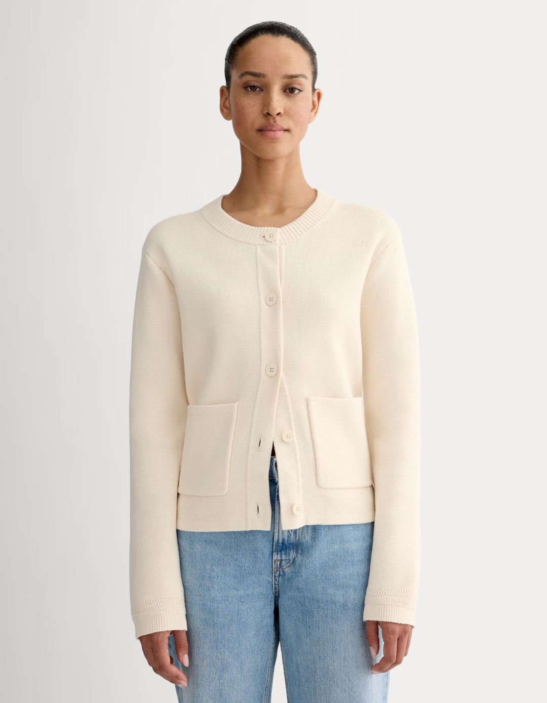 Person in a simple cardigan and jeans standing against a plain background; featured in shopping article