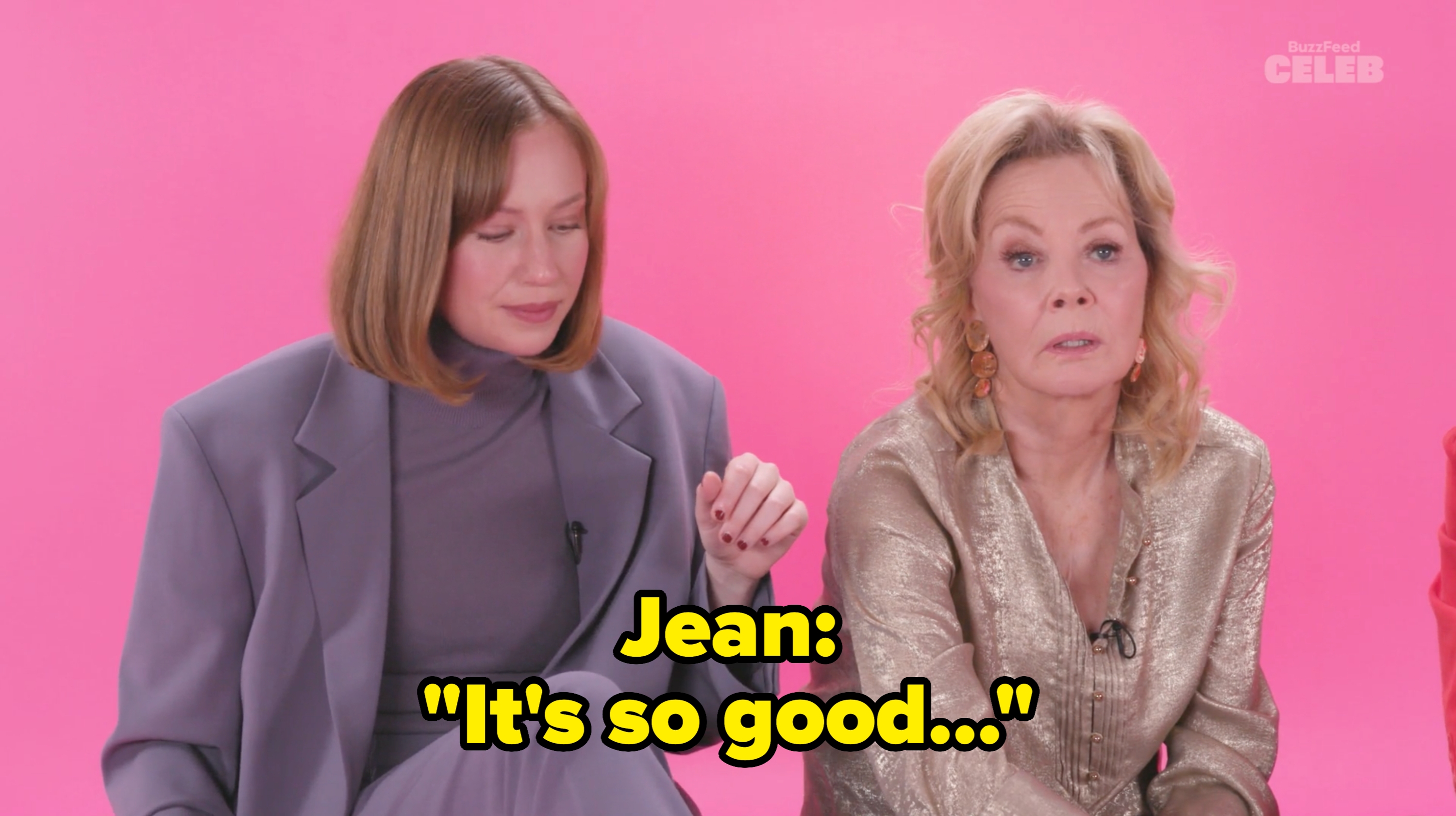 Two women seated against a solid backdrop. The woman on the left wears a modern suit, while the woman on the right is in a shimmery jacket